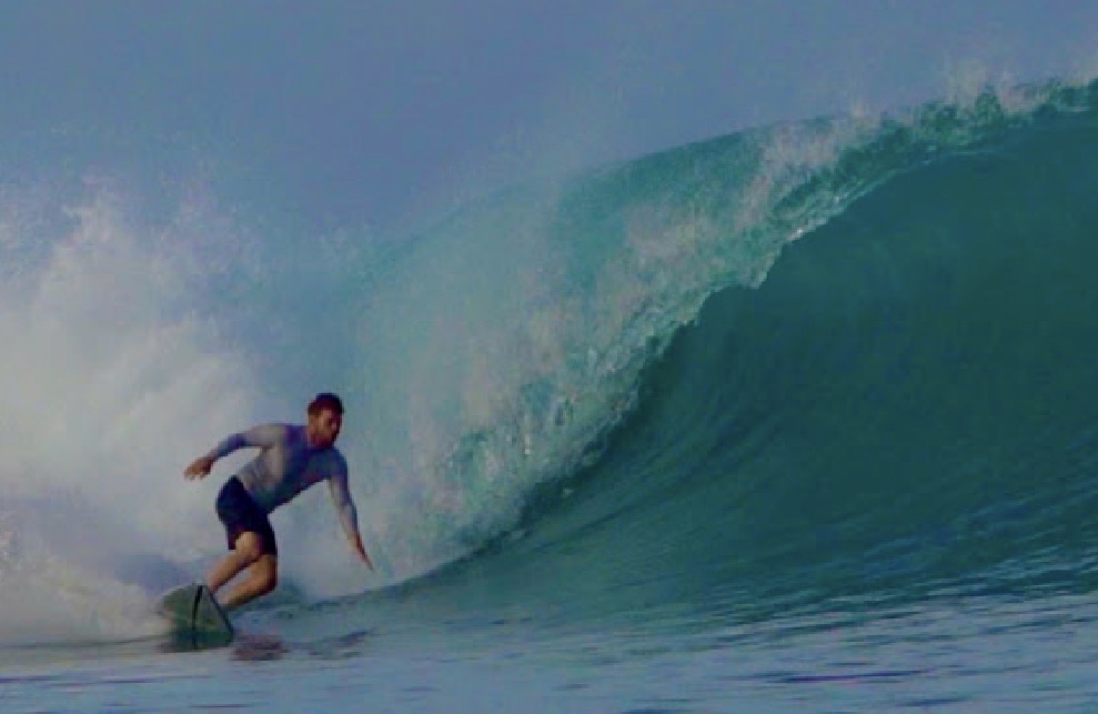 A surfer riding across a blue ocean wave